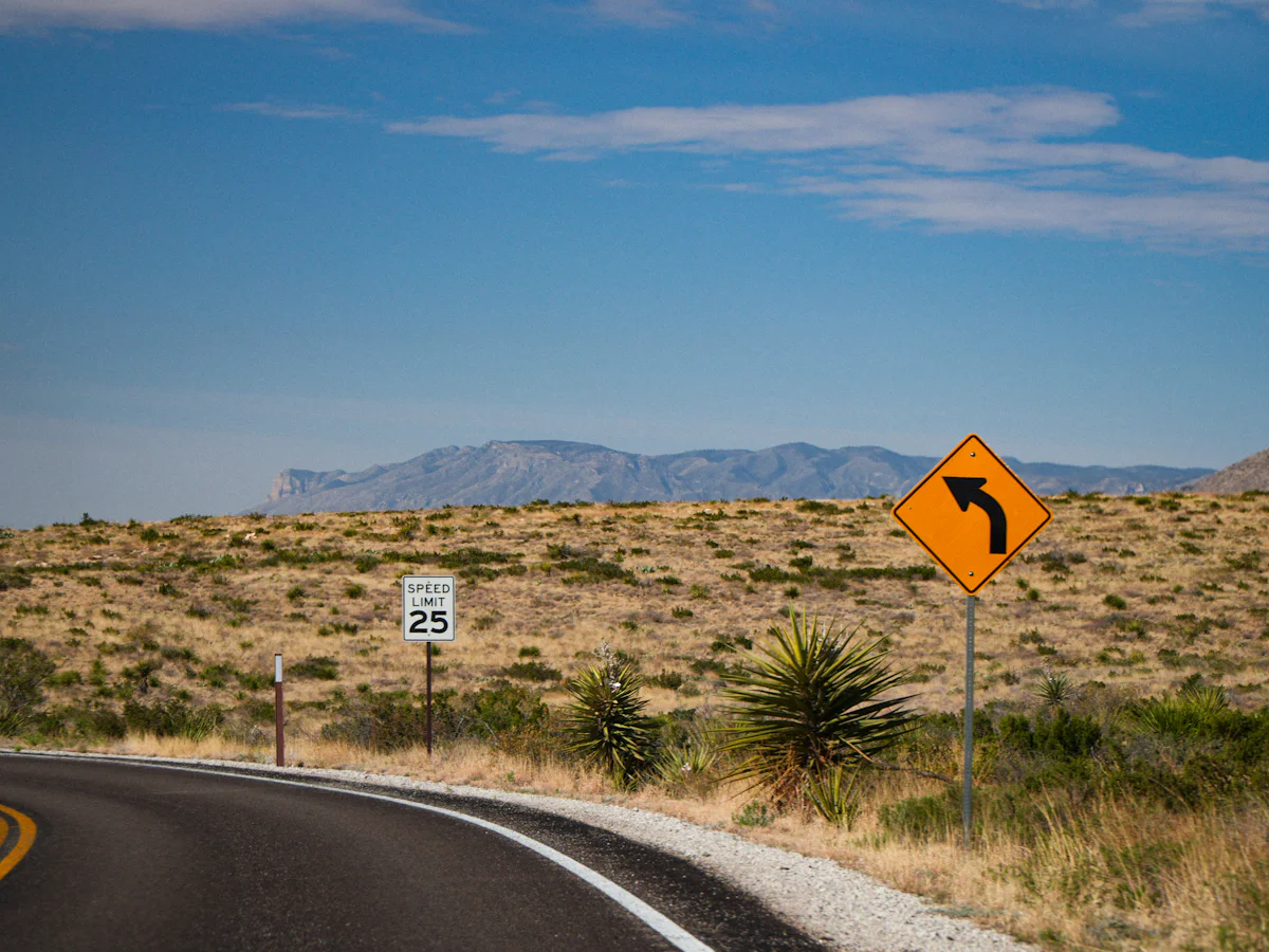 A two-lane road through a dry landscape with a yellow warning sign